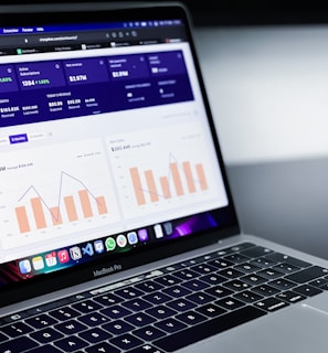 A laptop with an open screen displaying dashboard analytics featuring charts, graphs, and numerical data related to sales and subscriptions. The interface is predominantly dark-themed with sections highlighting key performance metrics. The device shown is a MacBook Pro, indicated by the keyboard layout and branding.